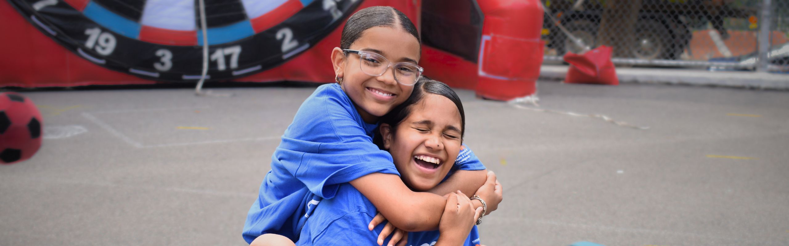 Two teenage girls embrace, smiling and laughing.