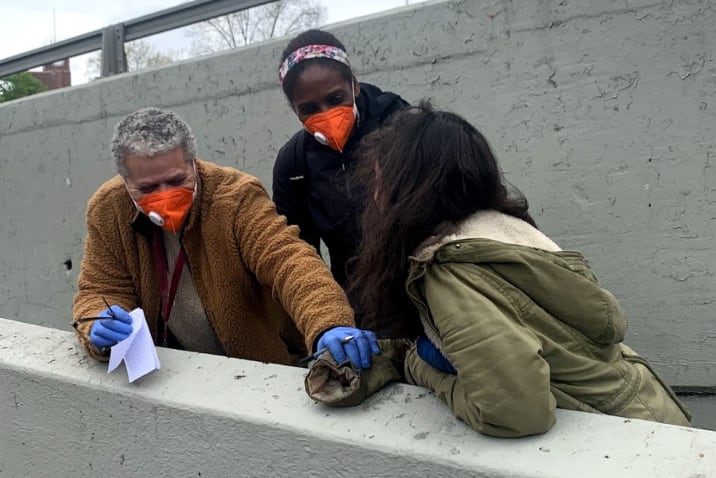 Two people wearing orange smiling and reaching out to a women in the homeless outreach team