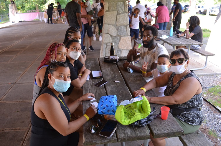 A group of people wearing masks sits at a picnic table.
