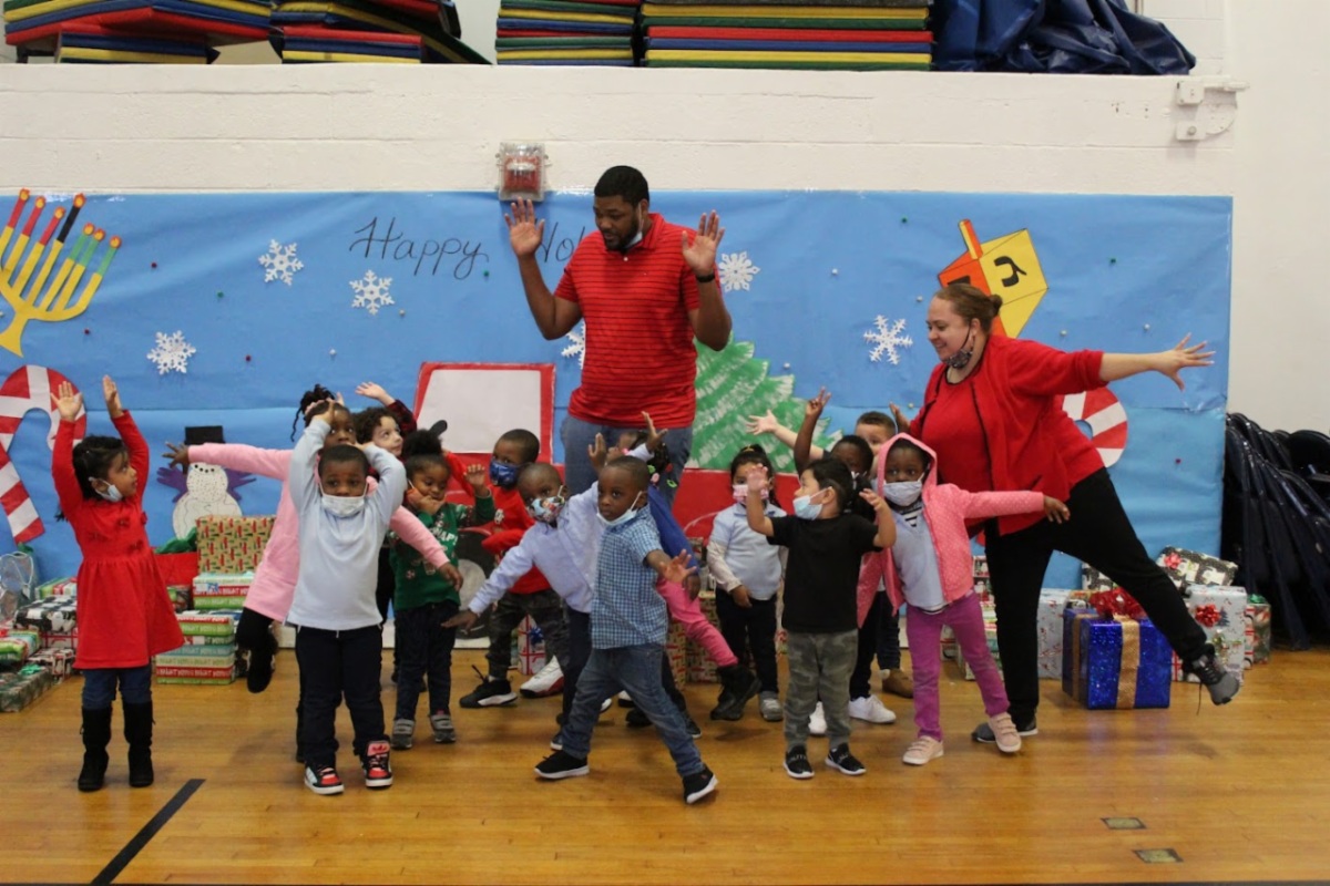 Young children and two counselors stand in a group with their hands up, celebrating the holidays