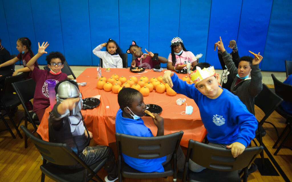 Children eating pizza sitting around a table filled with small pumpkins.