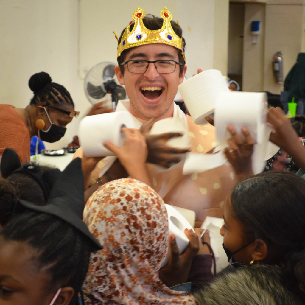 A young man wearing a crown getting turned into a toilet paper mummy.