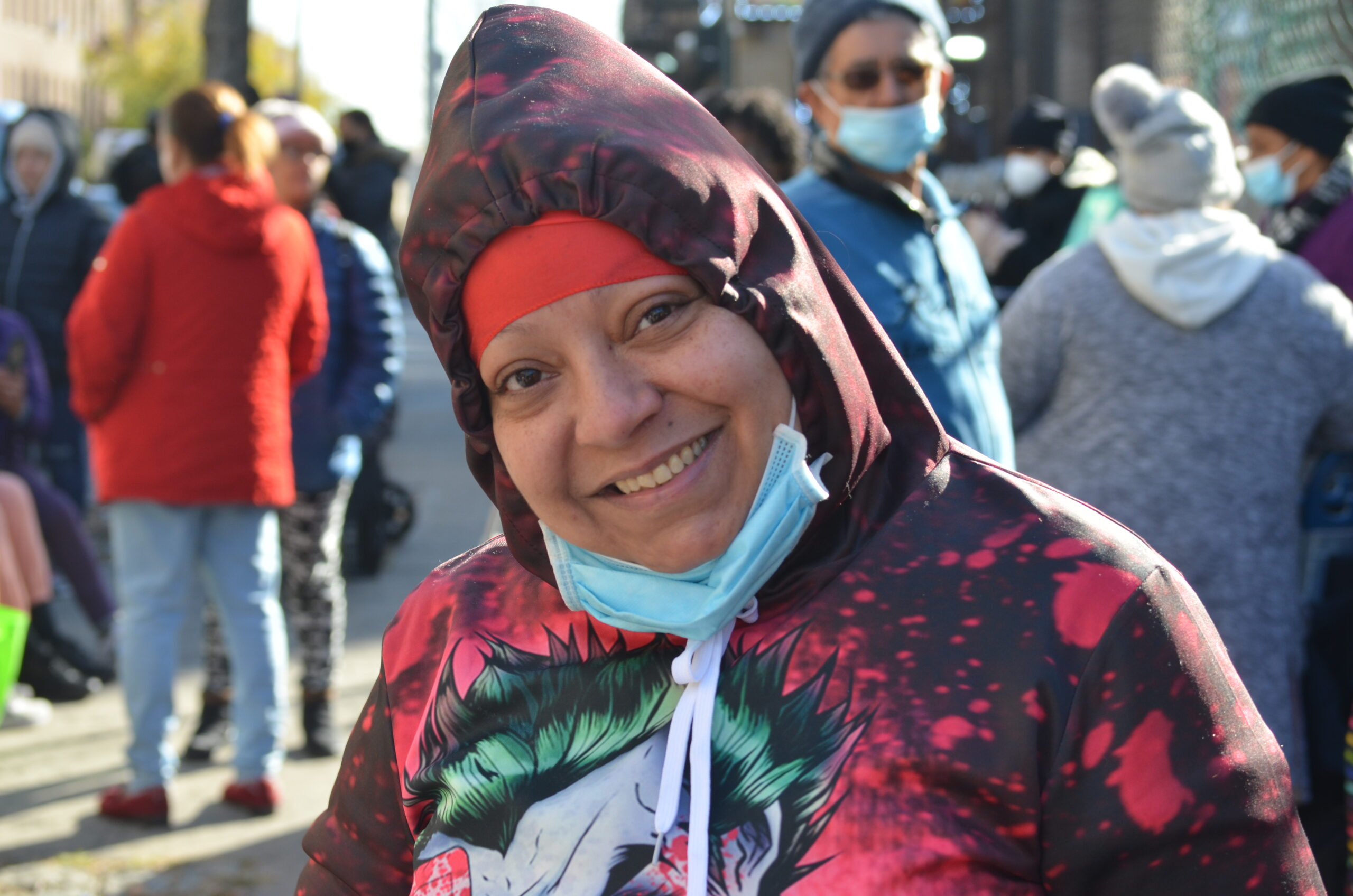 A woman wearing a hooded sweatshirt smiles while many people stand behind her in a line.