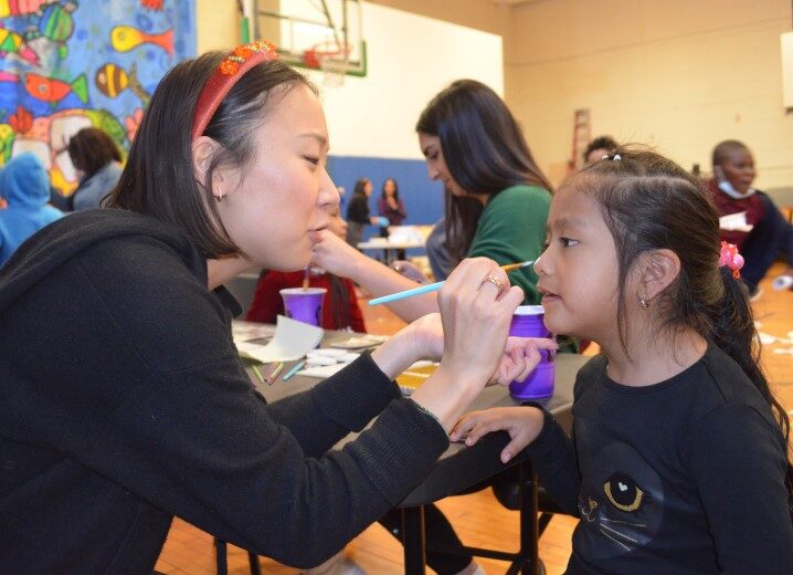 A young girl gets her face painted by a volunteer.