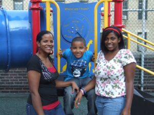 A mother and her two children stand together next to a playground.