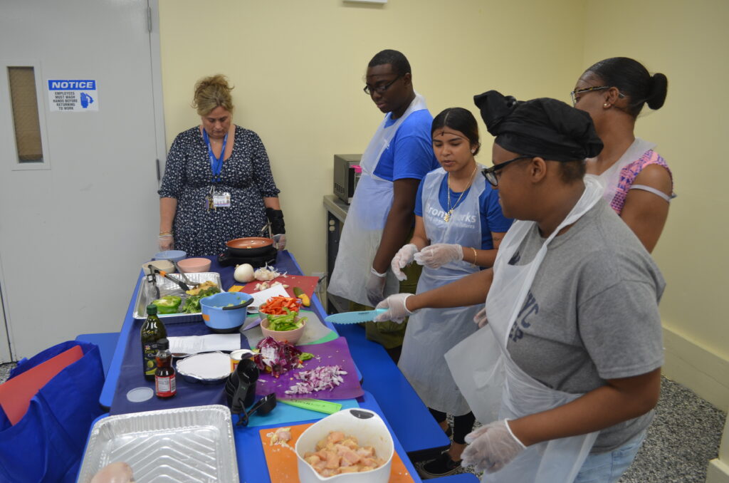 BronxWorks Community Health Program staff stand in front of bowls and cutting boards of food, preparing to cook a meal.