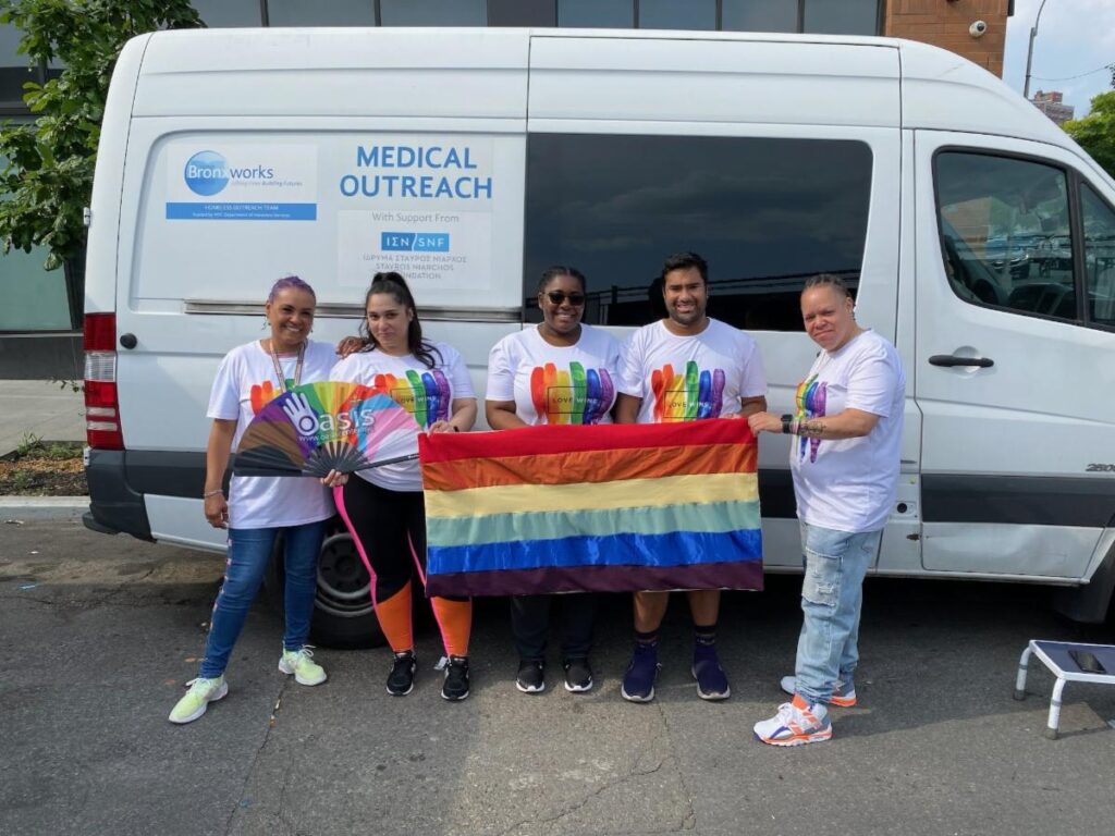 BronxWorks Staff wearing rainbow shirts and holding a rainbow pride flag. They are standing in front of the BronxWorks Medical Outreach van.
