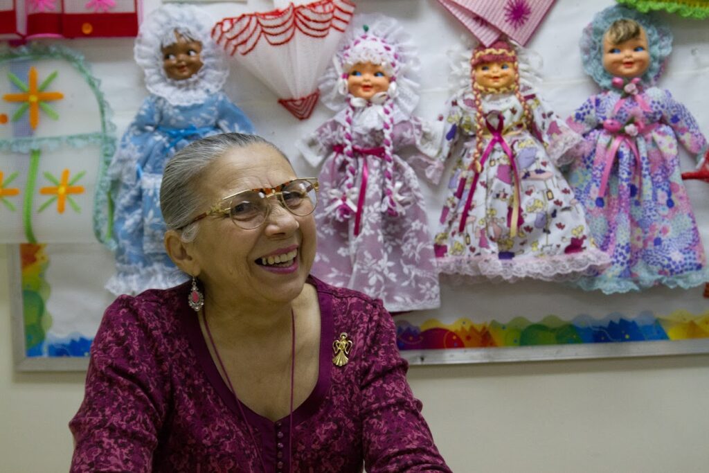 A woman sits in front of four dolls and smiles.