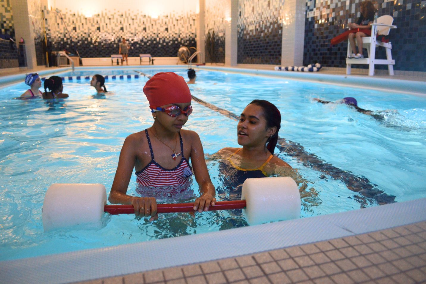 A young woman is teaching a young girl how to swim.