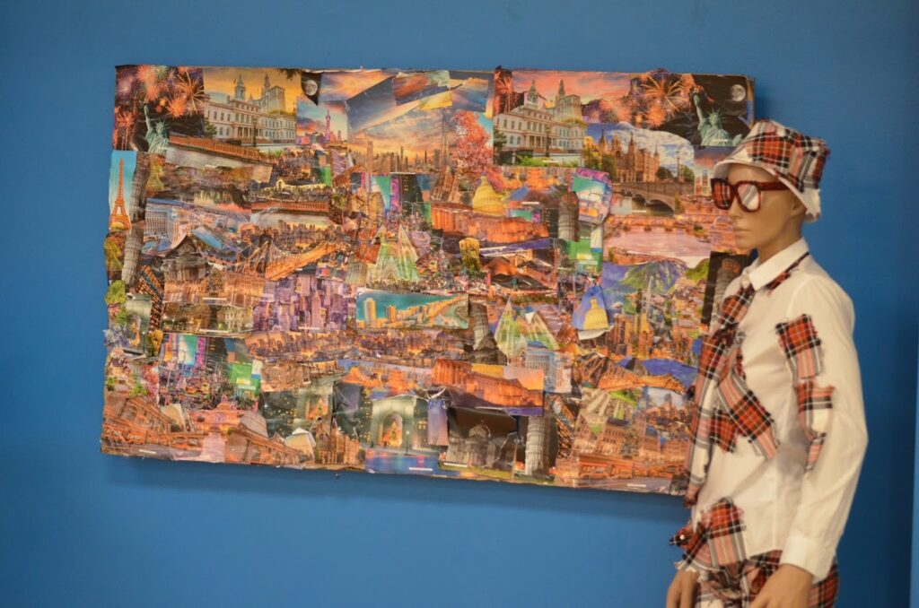 A mannequin wears a hat, glasses, and a shirt covered with swatches of red and green plaid flannel; the mannequin is flanked by a rectangular canvas plastered with images of all different colors.