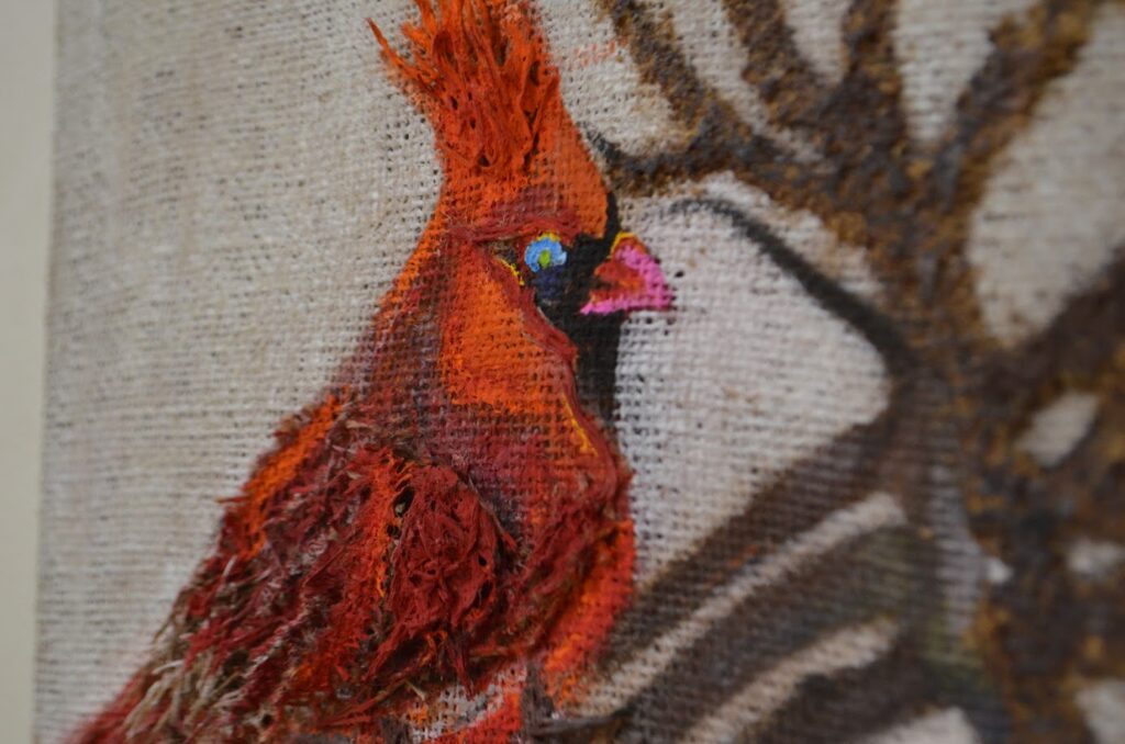 Painting of a cardinal. The cardinal bird is orange an red with a blue eye.