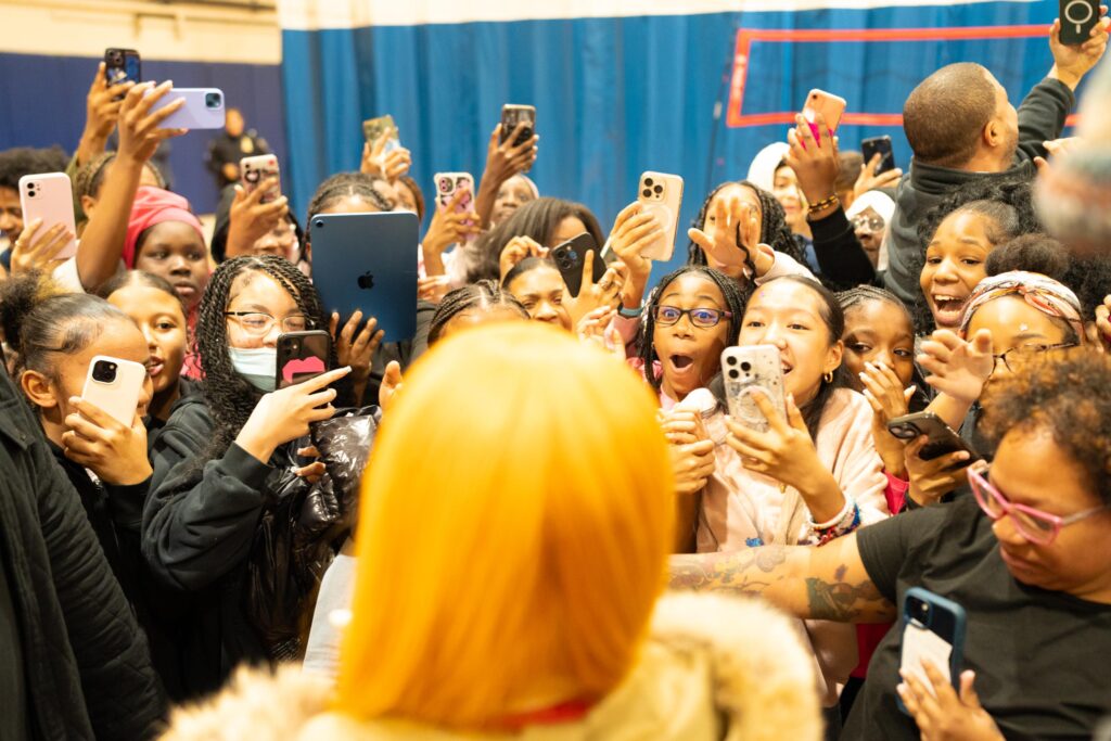 Many girls smile and cheer while taking pictures with their cell phones of a woman in the foreground