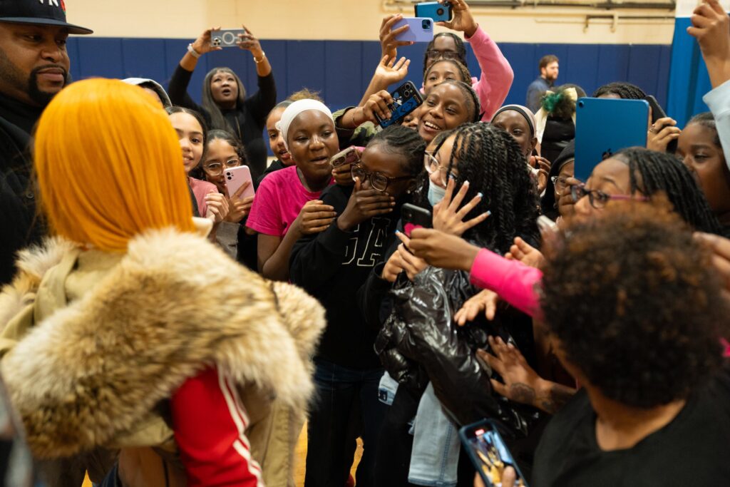 Many girls smile and cheer while taking pictures with their cell phones of a woman in the foreground