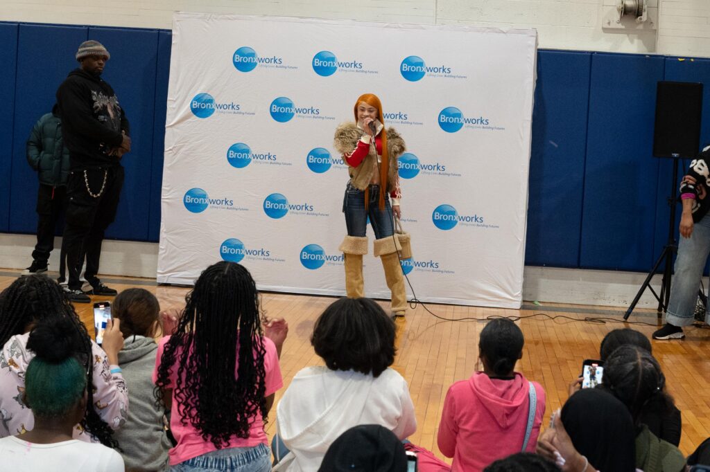 Rapper Ice Spice stands in front of a BronxWorks Step & Repeat and addresses a crowd.