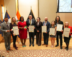 Many people stand together holding Citations of Merit from the Bronx Borough President.