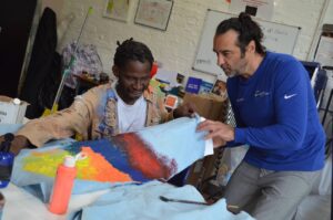 Two men work together on painting a piece of fabric.