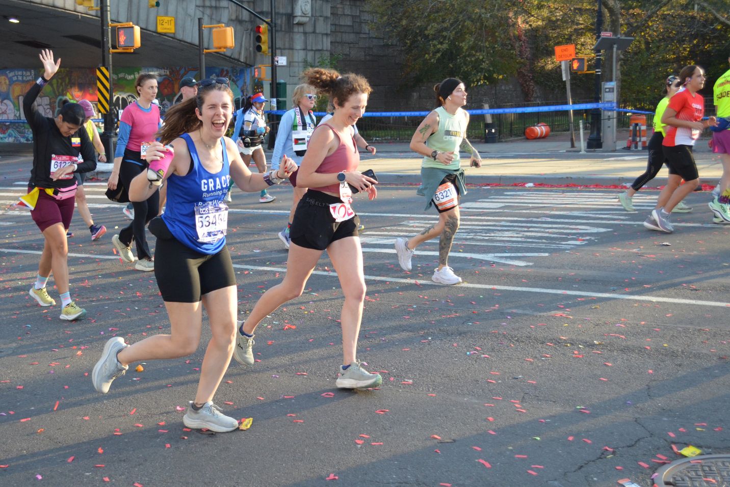 A woman is running in a blue sleeveless shirt. She has her fists raised and a big smile.